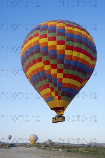 A colorful hot air balloon floats in daylight over a meadow under clear blue sky, Göreme National