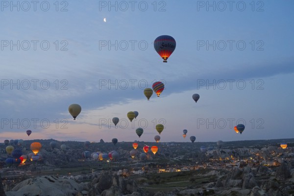 Many hot air balloons float at dusk over the picturesque landscape of Cappadocia, Göreme National
