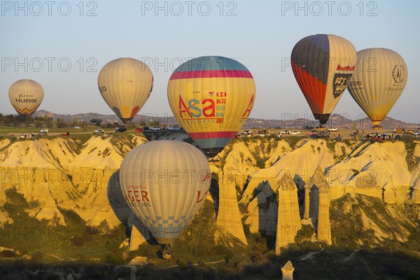 A group of balloons floats along a sunlit rock formation, hot air balloons, Göreme National Park,