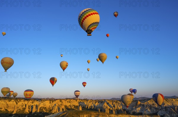 Hot air balloons float over rocks in a vast landscape in morning light, Göreme National Park,