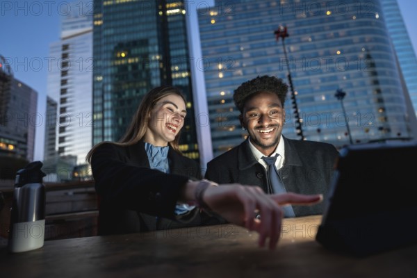 Diverse colleagues enjoying content on a digital tablet outdoors at night in an urban setting with