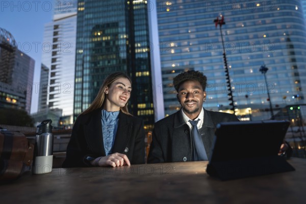 Diverse business colleagues working together on a digital tablet outdoors on a wooden table,