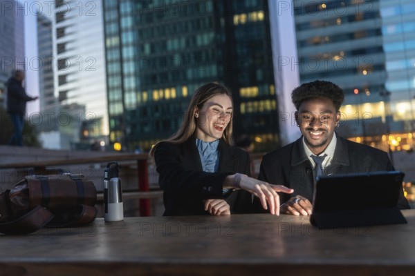 Two diverse business colleagues reviewing content on a digital tablet, discussing and laughing