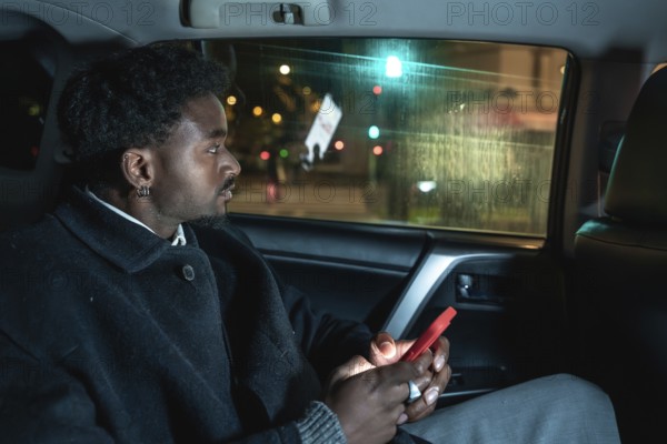 Afro american passenger riding in a car, looking out the window at city lights while holding a