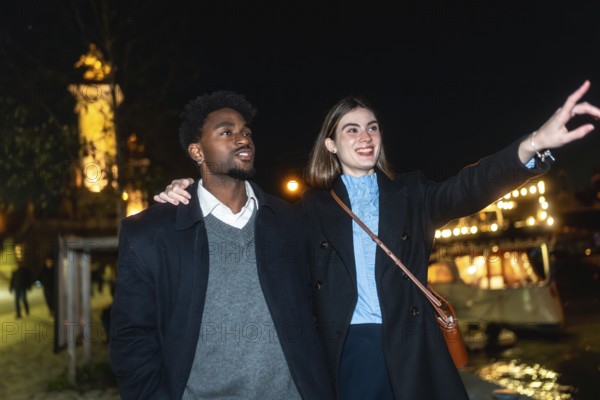 Young couple enjoying a romantic night out, with a woman pointing towards the city lights and a man