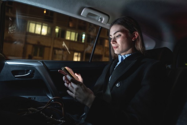 Young businesswoman commuting by car at night, focused on her smartphone as she scrolls messages