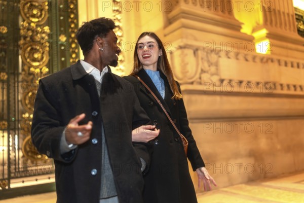 Smiling interracial couple enjoying a romantic night out, walking closely and conversing in front