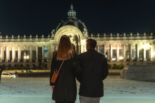 Couple is walking arm in arm, admiring an illuminated historical building with neoclassical