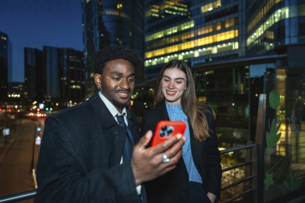 Diverse business colleagues reviewing content on a smartphone, standing outdoors at night with