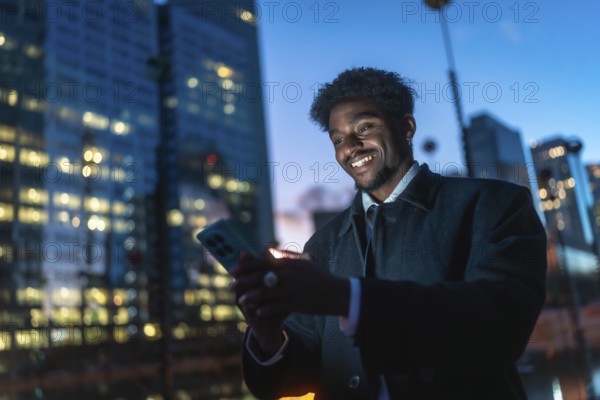 Young black man connecting with his smartphone, illuminated by the screen's glow, against a blurred