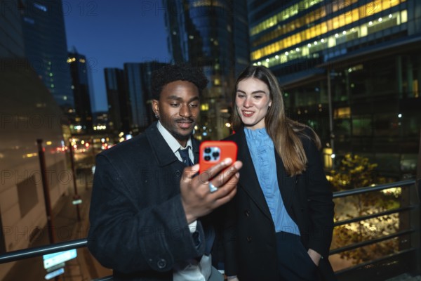 Diverse business professionals standing outside in a city at night, sharing content on a