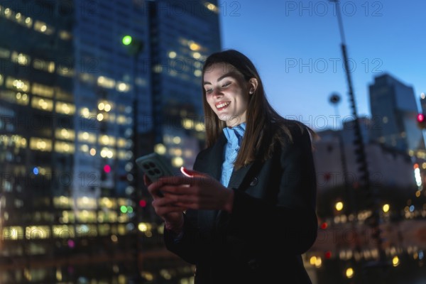 Woman smiling illuminated by smartphone screen, connecting and enjoying digital content outdoors in