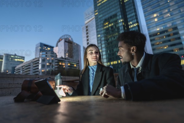 Two diverse business colleagues discussing ideas and working together on a digital tablet at night,