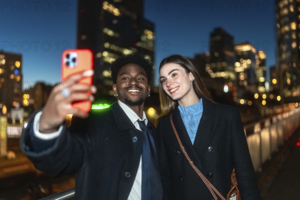 Diverse couple smiling, taking a selfie outdoors in an urban environment at night, capturing a