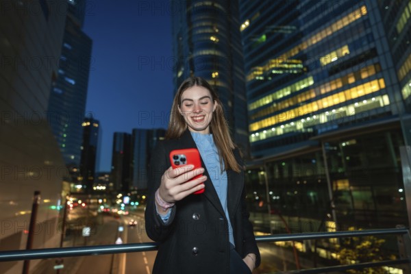 Young woman smiling while reading content on her red smartphone, enjoying digital communication and