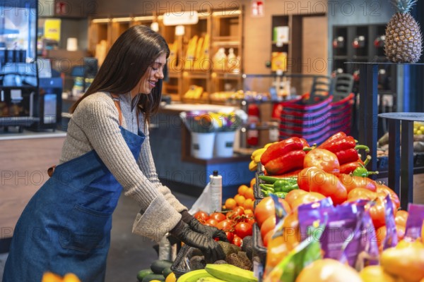 Happy young woman wearing an apron and gloves, organizing and stocking fresh fruits and vegetables