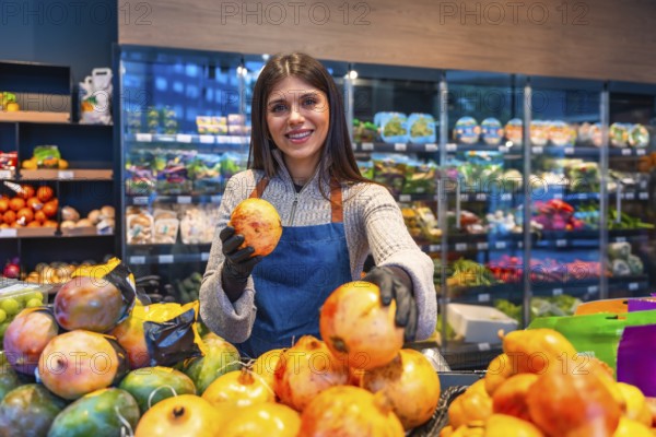 Smiling young woman greengrocer wearing an apron and gloves at a supermarket produce stand, proudly