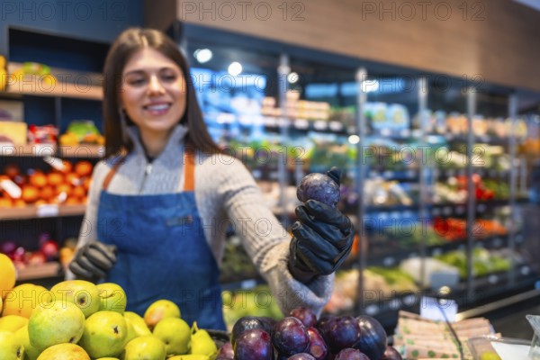 Smiling saleswoman in an apron and gloves working at a supermarket's produce section, holding a