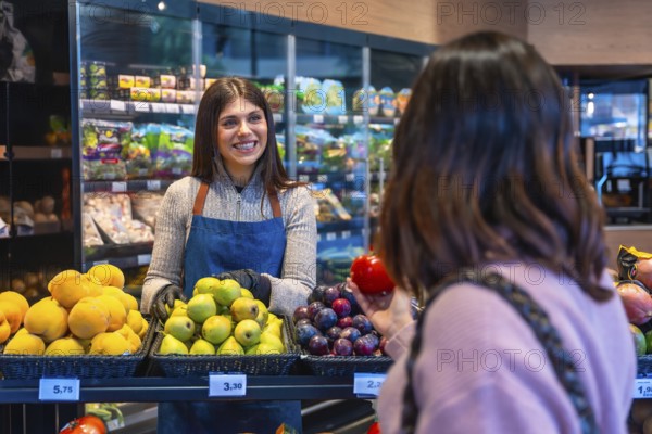 Smiling woman greengrocer assisting a customer choosing fresh organic fruit, including pears,