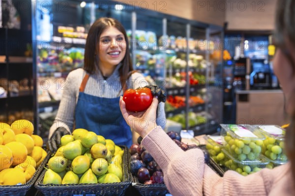 Greengrocer handing a ripe red tomato to a customer during grocery shopping in a produce section,