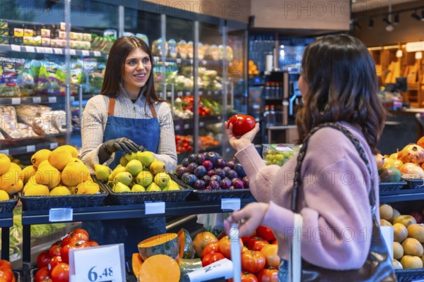 Friendly store employee warmly assisting a female customer selecting fresh organic produce at the