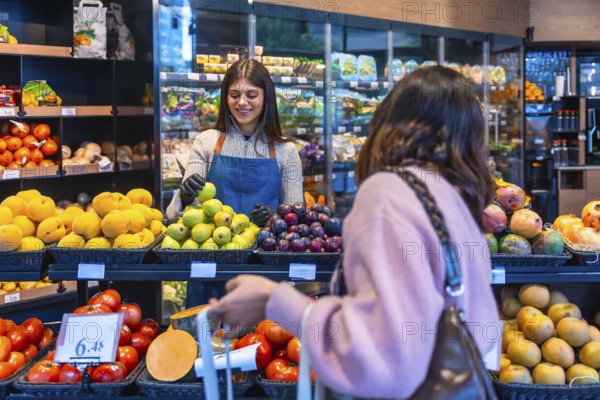 Friendly supermarket employee wearing an apron and gloves assisting a female customer in the