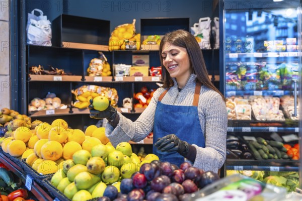 Smiling female greengrocer wearing an apron and gloves, carefully arranging fresh fruit on a