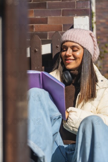 Woman smiling with closed eyes, wearing a beanie and headphones, sitting peacefully outdoors in the