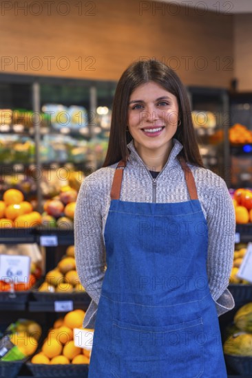 Young woman wearing a denim apron and a sweater, smiling confidently while standing in a