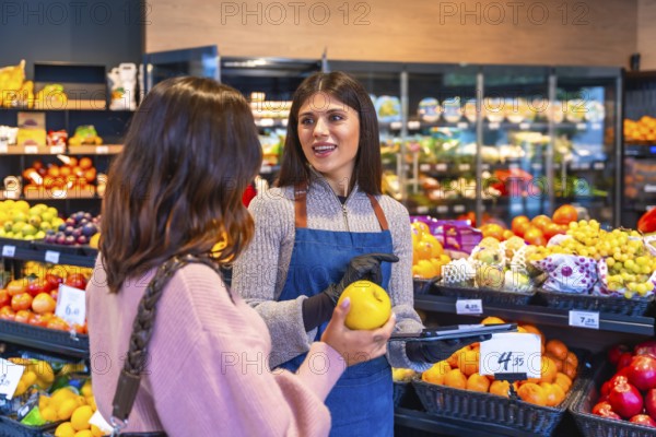 Supermarket employee wearing an apron and gloves helping a woman consumer select a fresh yellow