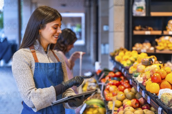 Female shop assistant wearing an apron and gloves managing fresh fruit and vegetables inventory