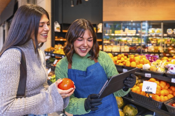 Store employee in an apron and gloves using a tablet while helping a smiling customer holding a