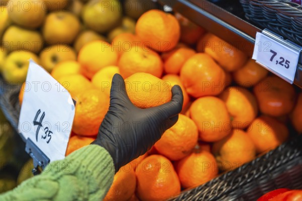 Person wearing a protective glove picking an orange from a large display of citrus fruits in a