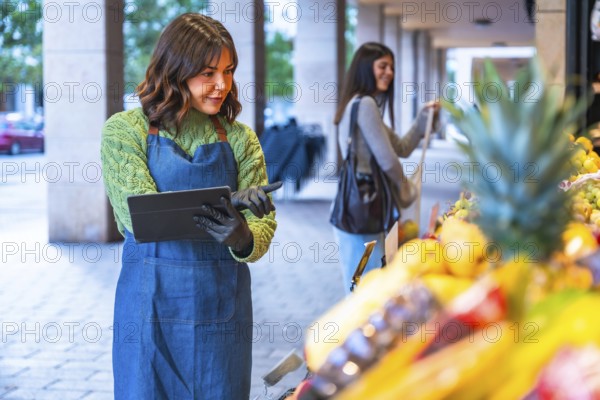 Female small business owner wearing an apron and gloves managing inventory and sales on a digital