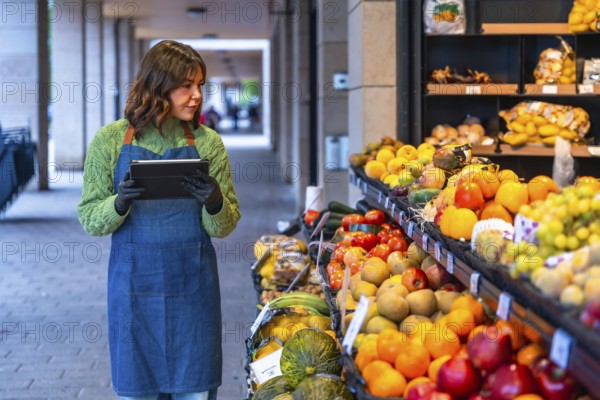 Woman grocer using a digital tablet to manage inventory and fresh produce at her outdoor fruit and