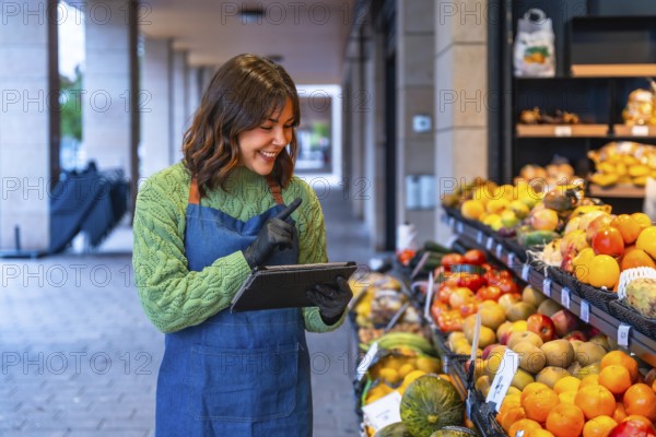 Woman in an apron and gloves managing fresh produce at her small business, using a digital tablet