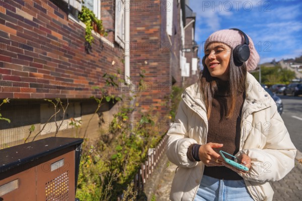 Young woman smiling and listening to music through headphones while walking outdoors on an urban