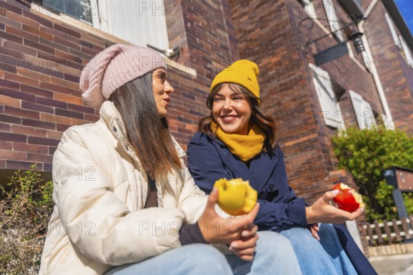 Two young women friends sitting together on a sunny autumn day, enjoying fresh apples while having