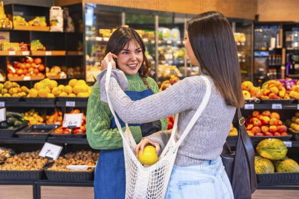 Friendly supermarket employee smiling and assisting a customer holding a reusable net bag to put