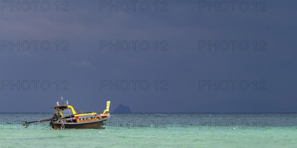 Longtail boat (Thai: Ruea Hang Yao) on the beach, behind it an approaching thunderstorm, Koh Ngai