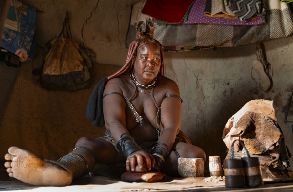 Elderly Himba woman making red paste for skin care, in a hut, traditional Himba village, Kaokoveld,
