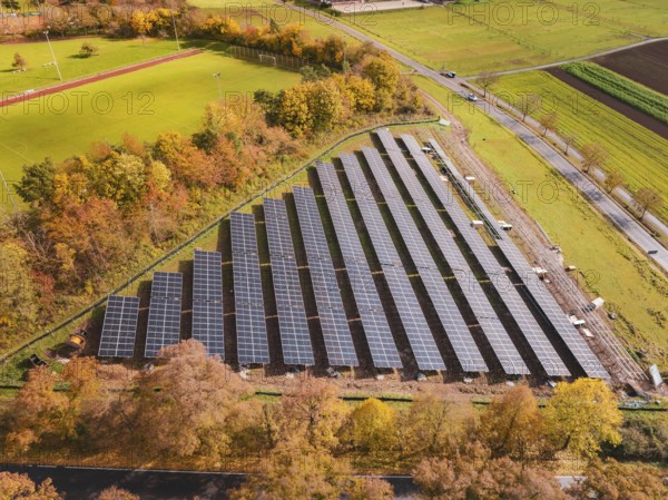 Solar systems next to a sports field, surrounded by autumn-colored trees, Bau PV Freifaechenanlage,