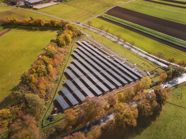 Aerial view of solar panels surrounded by autumn trees and green fields, Bau PV Freifaechenanlage,