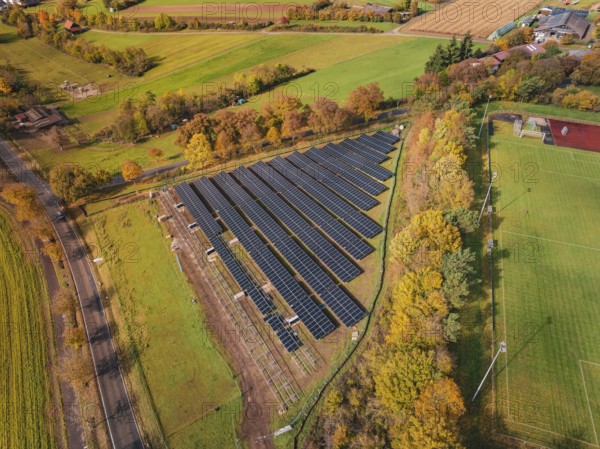 Aerial view of a solar field in an autumn landscape with fields and colorful trees, PV
