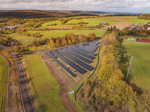 Large solar field in an autumn landscape, surrounded by green fields and trees, Bau PV