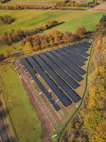 Panoramic aerial view of a solar plant surrounded by green fields and autumn trees, PV open-air