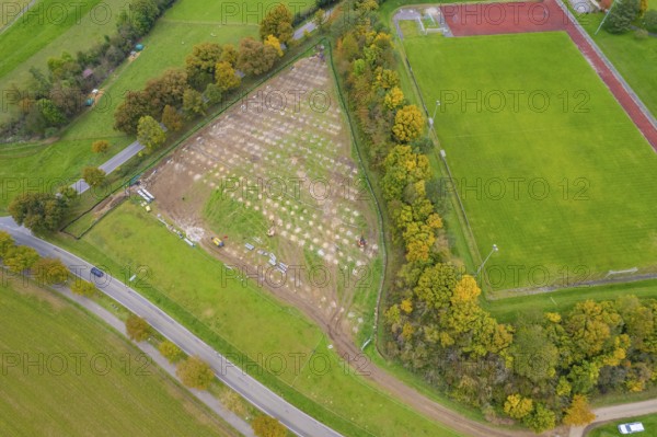 Aerial view of a large field next to a sports field, surrounded by autumn trees and roads, PV