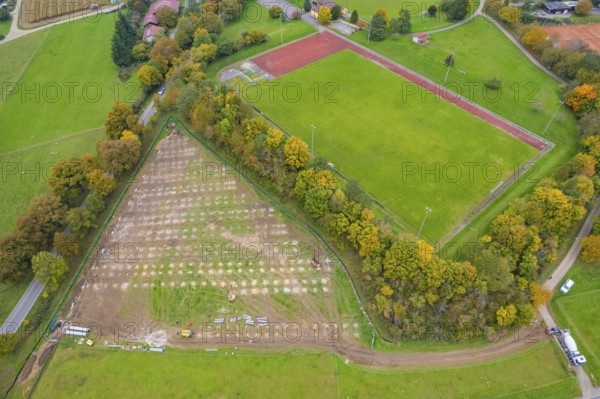 Aerial view of a sports field next to a large field and surrounded by autumn trees, PV