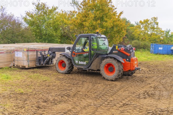 A forklift truck transports boxes across muddy soil in an autumn environment, Bau PV