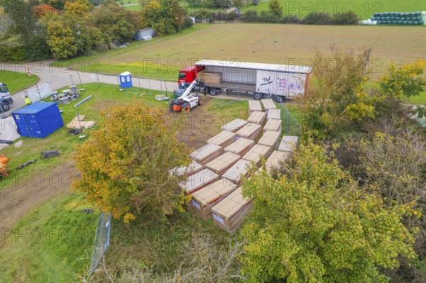 A forklift truck moves boxes next to a truck in a green autumn landscape, Bau PV Freifaechenanlage,